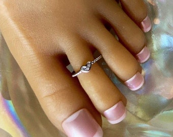 May include: A silver toe ring with a small heart-shaped charm set with clear cubic zirconia stones.