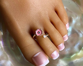 May include: A silver toe ring with a pink flower design and a small clear rhinestone. The ring is adjustable and can be worn on any toe.