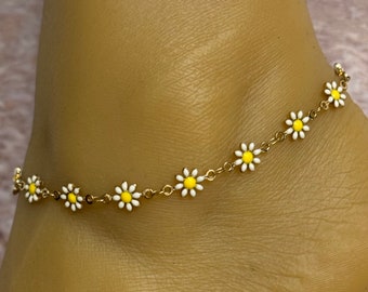 May include: A gold chain ankle bracelet with white and yellow daisy charms.
