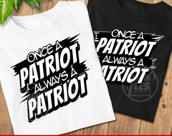 May include: Two t-shirts, one white and one black, with the text "ONCE A PATRIOT ALWAYS A PATRIOT" in a bold, black and white design. The shirts are displayed on a wooden surface.