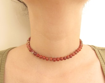 May include: A red and brown beaded choker necklace on a person's neck.