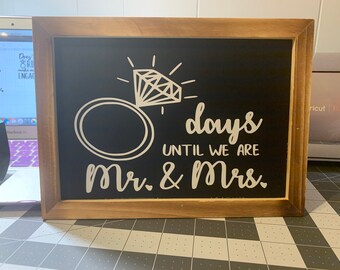 May include: A framed chalkboard sign with a wooden border. The black chalkboard features white text and a diamond ring graphic. The text reads "0 days until we are Mr. & Mrs.", perfect for a wedding countdown.