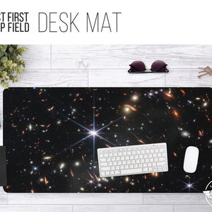 May include: A black desk mat with a space-themed design featuring a bright star and many galaxies. The text "JWST FIRST DEEP FIELD" is at the top of the mat.