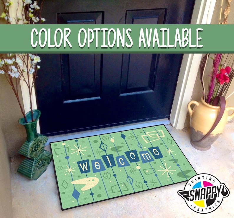 May include: A green welcome mat with a retro design featuring a stylized welcome message, geometric shapes, and stars. The mat is placed in front of a black door.
