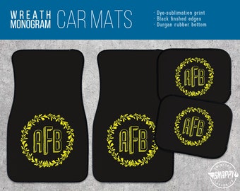 May include: Black car floor mats with a yellow wreath monogram design. The monogram reads "AFB".