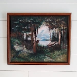 May include: A framed painting depicting a forest scene with a view of a lake and mountains in the distance. The painting is done in shades of green, brown, and blue.