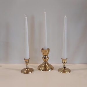 May include: Three gold candle holders with white candles. The candle holders are different sizes and styles.