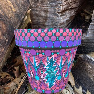 May include: A hand-painted terracotta flower pot with a colorful mandala design featuring a lightning bolt in the center. The pot is decorated with pink, purple, blue, and teal dots.