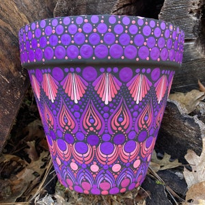 May include: A purple and pink hand-painted terracotta flower pot with a geometric pattern. The pot is decorated with dots and swirls.