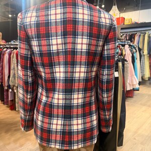 May include: A long-sleeved blazer featuring a plaid pattern in red, navy blue, and off-white. The garment has a structured collar, a centre back seam, and three small buttons on each sleeve cuff, displayed on a mannequin torso.