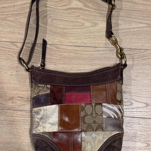 May include: A multi-textured patchwork crossbody bag featuring various brown, tan, metallic gold, red, and zebra-print panels. The bag includes a dark brown leather top trim, a zipper closure, and an adjustable brown leather shoulder strap with brass hardware.