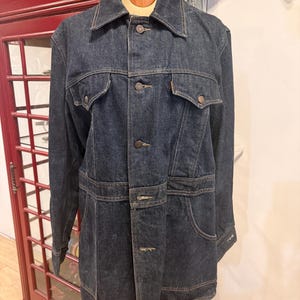 May include: A dark wash denim jacket with a button-down front, two chest pockets, and two hip pockets. The jacket has a collared neckline and long sleeves. The jacket is displayed on a mannequin.