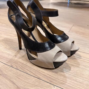 May include: A pair of high-heeled sandals with a platform sole. The shoes feature a combination of black leather and beige suede, with a snakeskin-textured accent on the toe and heel. The heels are approximately 4 inches (10 cm) tall.
