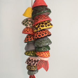 May include: A colorful ceramic fish mobile with a red, yellow, green, and black pattern. The fish is made of multiple pieces that are strung together.