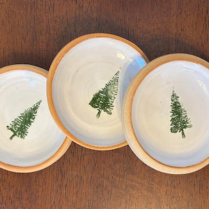 May include: Three small white ceramic dishes with a brown rim. Each dish has a green tree design.