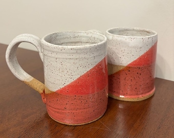 May include: Two ceramic mugs with a speckled white glaze and a geometric design of pink and tan stripes.