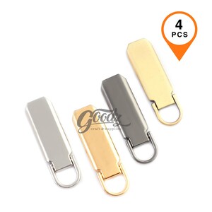 May include: A set of four rectangular zip pulls in silver, gold, gunmetal, and light gold finishes. Each pull features a smooth, flat metal body with a rounded bottom and a small attached circular ring. An orange graphic indicates 4 PCS.