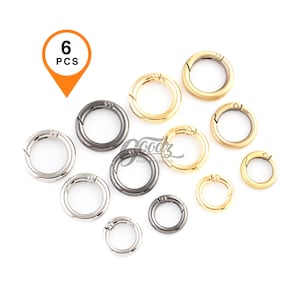 May include: A collection of round metal spring clasp rings in silver, gold, and gunmetal gray. The image shows a variety of sizes, with a total of six pieces. The clasps are arranged on a white background.