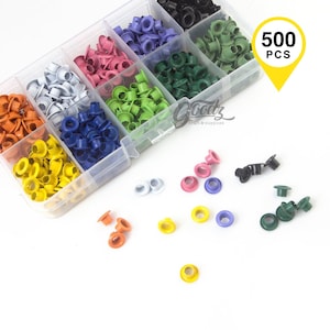 Puede incluir: Un organizador de plástico transparente lleno de ojales metálicos de colores en varios tonos, incluyendo naranja, amarillo, azul, rosa, verde y morado. La imagen incluye una etiqueta amarilla que dice "500 PCS".