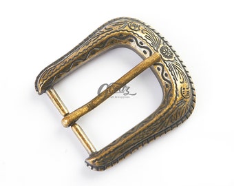 May include: A brass-toned metal belt buckle featuring an antiqued finish and intricate engraved floral and scroll patterns along the frame. The buckle includes a central prong and a rectangular shape with rounded corners, displaying a weathered texture.