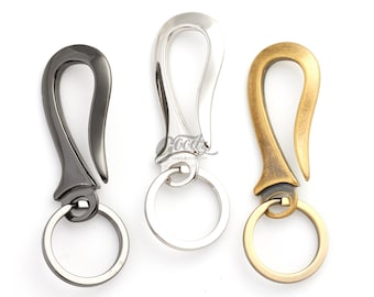 Pode incluir: Três chaveiros com diferentes acabamentos: preto, prata e dourado. Cada chaveiro tem um design em forma de gancho e um anel circular.