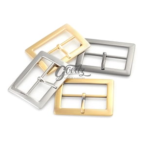 Może przedstawiać: Trzy metalowe klamry do paska w różnych wykończeniach: złote, srebrne i brązowe. Klamry są prostokątne z centralnym prętem i dwoma zębami.