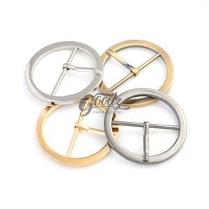 May include: Four metal belt buckles in different finishes: silver, gold, and two shades of antique silver. The buckles are round and have a simple, classic design.