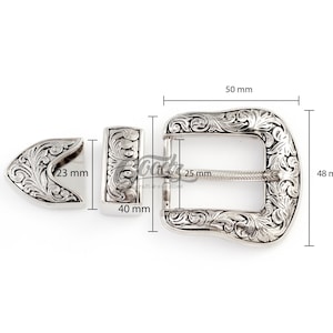 May include: Silver-toned metal belt buckle with an ornate floral design. The buckle measures 2 inches wide by 1.9 inches tall. The buckle is made up of two pieces, a main buckle and a separate prong.