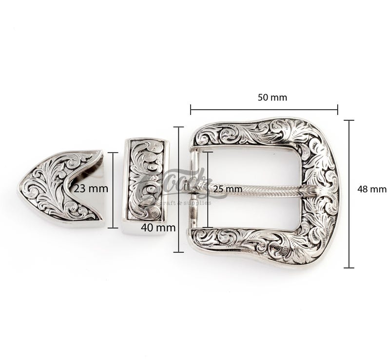 May include: Silver-toned metal belt buckle with an ornate floral design. The buckle measures 2 inches wide by 1.9 inches tall. The buckle is made up of two pieces, a main buckle and a separate prong.
