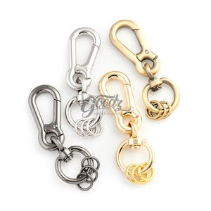 May include: Four metal swivel lobster claw clasps with attached split rings, arranged in a cluster. The clasps are finished in gunmetal, silver, light gold, and brass tones. Each clasp features a spring-loaded gate and a rotating swivel base.