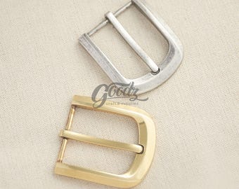 May include: Two belt buckles, one with a brushed silver finish and one with a polished gold finish. Both buckles feature a rounded rectangular frame and a central prong. The text Goodz craft & supplies is printed in black between the two buckles.