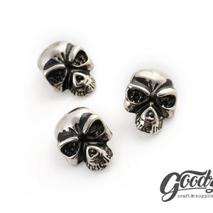 Può includere: Tre bottoni a forma di teschio argentati con dettagli neri per gli occhi.