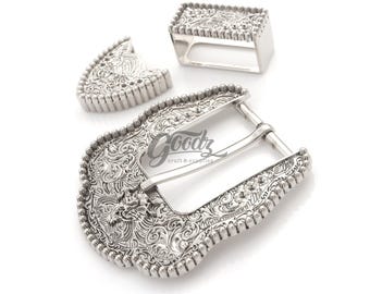 May include: Silver-toned metal belt buckle set with intricate floral and scrollwork designs. The set includes a large buckle, a belt loop, and a smaller decorative piece. The word "Goodz" is printed on the buckle.