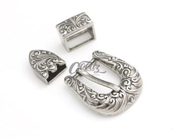 May include: A set of three silver-colored metal belt hardware pieces. The set includes a rectangular loop, a decorative tip, and a horseshoe-shaped buckle, all with an ornate, swirling floral design.