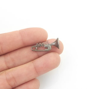 Puede incluir: Un imperdible de color plateado en forma de trompeta. El imperdible está abierto y listo para usarse.