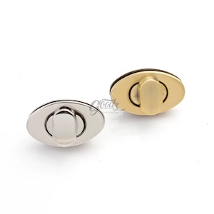 May include: Two oval-shaped purse clasps. One is silver-toned, the other is gold-toned. Each clasp has a central bar that pivots to open and close. The clasps are designed for use in bag making and other craft projects.