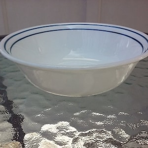 May include: A white ceramic bowl with a blue rim and two blue lines around the top. The bowl is sitting on a glass table.