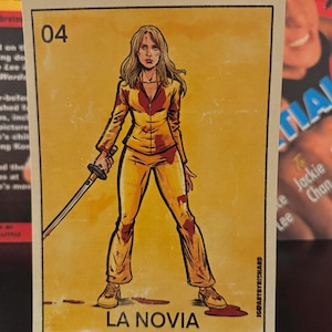 May include: A stylized illustration of a woman in a yellow jumpsuit holding a sword, with blood stains. The image is a card with the number 04 and the text "LA NOVIA". The background is yellow.