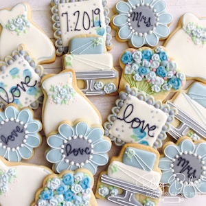 May include: Assortment of decorated sugar cookies with blue and white icing. The cookies feature various designs including wedding dresses, flowers, cakes, and the words "love" and "Mrs.".