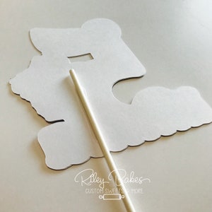 May include: White cake topper with a cutout design of a butterfly. The topper is attached to a white stick.