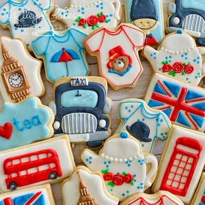 May include: A collection of decorated sugar cookies featuring British themes, including a red double-decker bus, a black taxi, a teapot, a Union Jack flag, and a Big Ben clock tower. The cookies are decorated with colorful icing and details.