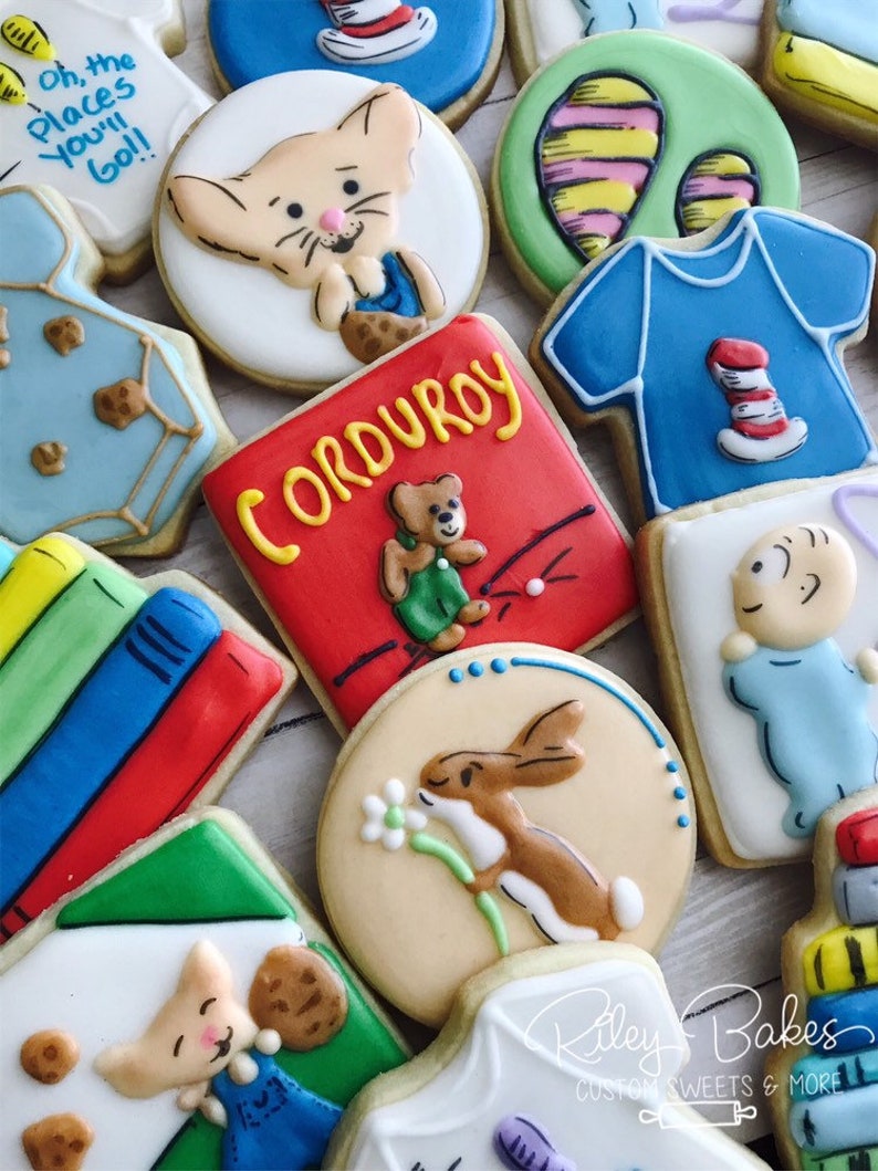 May include: A collection of decorated sugar cookies featuring children's book characters, including Corduroy, The Cat in the Hat, and Peter Rabbit. The cookies are decorated with colorful icing and details.