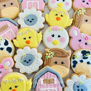 May include: A collection of farm animal themed sugar cookies decorated with colorful frosting. The cookies feature a variety of animals, including cows, pigs, chickens, horses, and sheep. The cookies are decorated with flowers, swirls, and other details. The cookies are arranged on a white surface. The text "Riley Bakes Custom Sweets & More" is visible in the bottom right corner of the image.