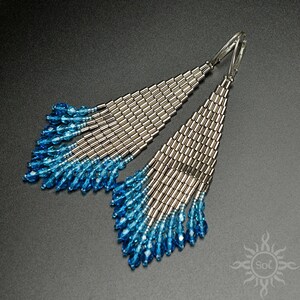 May include: A pair of long, silver and blue beaded earrings. The earrings are made with small, silver beads and blue crystal beads. The earrings are shaped like a teardrop and hang down to the shoulders.