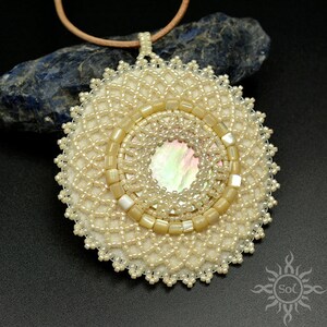 May include: A white beaded pendant with a circular design and a mother-of-pearl center. The pendant is attached to a brown leather cord.