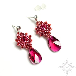 Op de afbeelding: Een paar oorhangers met een rood, stervormig kralenpatroon en een traanvormige roze kristallen hanger.