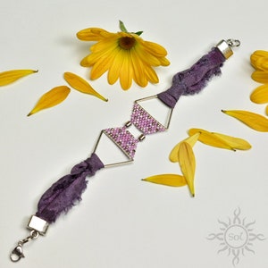Pode incluir: Um bracelete de tecido roxo com um design de contas geométricas prateadas. O bracelete é acentuado com um fecho prateado e é rodeado por pétalas de flores amarelas.