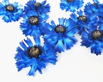 May include: A collection of ten blue artificial flowers with brown centers. The flowers are arranged in a cluster on a white background.
