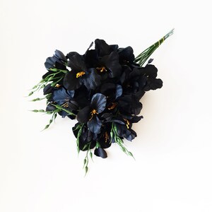 May include: A bouquet of black silk flowers with green stems and yellow centers. The flowers are arranged in a loose, natural style.