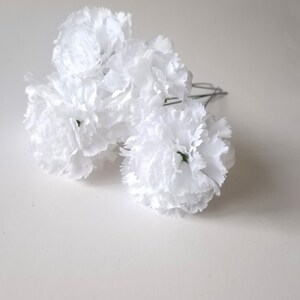 May include: A bunch of white carnations with green stems, arranged in a cluster. The carnations are artificial and have a realistic appearance.
